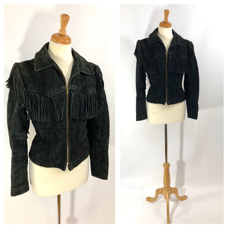 May include: A black suede jacket with fringe detailing on the shoulders and front. The jacket has a zipper closure and long sleeves.