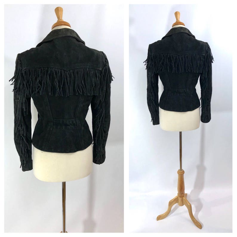 May include: Black suede jacket with fringe detailing on the sleeves and around the collar. The jacket has a fitted silhouette and a cinched waist.