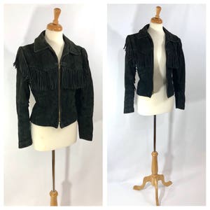 May include: A black suede jacket with fringe detailing on the shoulders and front. The jacket has a zipper closure and long sleeves.
