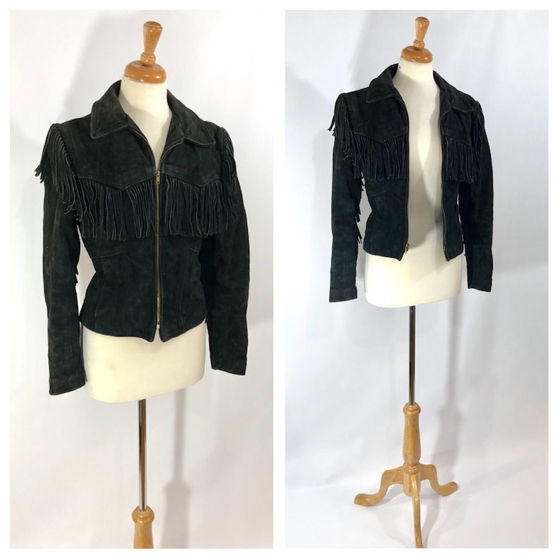 May include: A black suede jacket with fringe detailing on the shoulders and front. The jacket has a zipper closure and long sleeves.