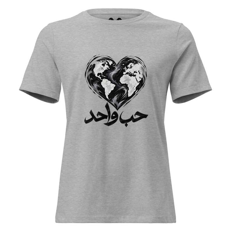 May include: A heather gray short-sleeve t-shirt featuring a black and white graphic of a heart-shaped world map. Below the heart, the Arabic text "حب واحد" is printed in a bold, black, stylized calligraphic font across the chest area.