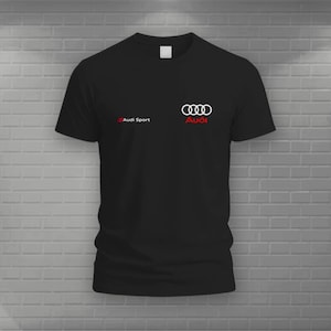 May include: A black short-sleeved t-shirt featuring the white Audi logo with the red Audi wordmark underneath, and the text Audi Sport in white with a small red square icon positioned to the left on the chest area of the garment.