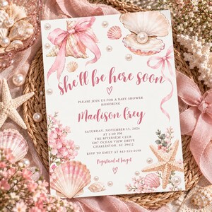 May include: A white baby shower invitation card featuring watercolor illustrations of pink seashells, a pearl in an open shell, a starfish, and pink floral accents. The text reads: she'll be here soon, Madison Grey, Saturday, November 15, 2026, at 2:00 PM, The Riverside Club, 1287 Ocean View Drive, Charleston, SC 29412, RSVP to Emily at 843-555-0198, Registered at Target.