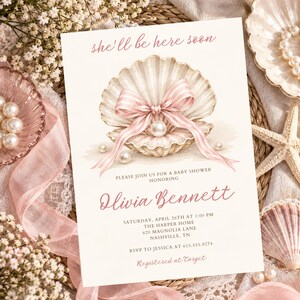 May include: A rectangular baby shower invitation card featuring a watercolor illustration of an open seashell with a pearl inside, tied with a pink striped ribbon. The text reads: she'll be here soon, PLEASE JOIN US FOR A BABY SHOWER HONORING Olivia Bennett, SATURDAY, APRIL 26TH AT 1:00 PM, THE HARPER HOME, 620 MAGNOLIA LANE, NASHVILLE, TN, RSVP TO JESSICA AT 615.555.9274, Registered at Target.