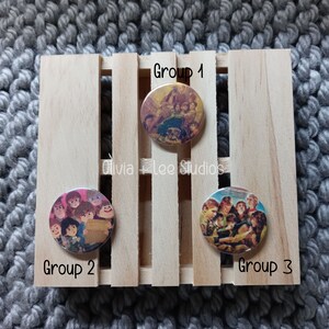 May include: Three round buttons with images of groups of people. The buttons are on a wooden crate with the words "Group 1", "Group 2", and "Group 3" printed below each button.