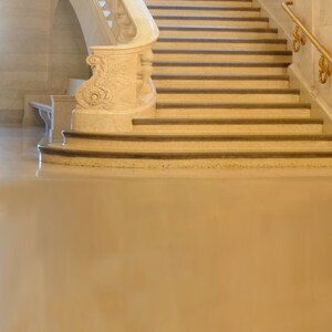 May include: A white marble staircase with a decorative railing and a gold handrail. The staircase is in a building with large windows.