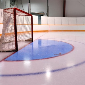 May include: A red hockey goal net sits on a white ice rink with a blue face-off circle and a white line.