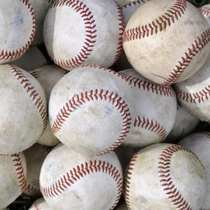 May include: A pile of white baseballs with red stitching. The baseballs are arranged in a random pattern and are slightly worn.