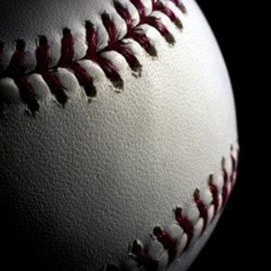 May include: Close-up of a white baseball with red stitching. The baseball is lit from the left, creating a shadow on the right side.