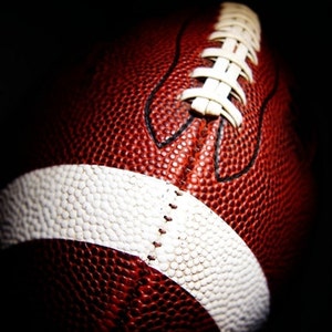 May include: Close-up of a brown and white football with white laces. The football is textured and has a white stripe around the middle.