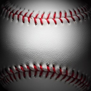 May include: Close-up of a white baseball with red stitching. The ball is slightly deflated and has a textured surface.
