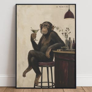 May include: A framed wall art print titled LE MARTINI featuring a chimpanzee sitting on a stool at a bar. The chimpanzee holds a martini glass with an olive. A dark red pendant light hangs above, and a cocktail shaker sits on the bar counter.