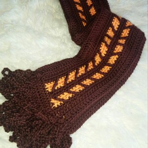 May include: A brown crocheted scarf with orange and yellow leaf-shaped details and brown fringe.