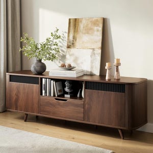 May include: A dark wood media console featuring two side cabinets with vertical slat detailing, a central open shelf, and a single drawer. The unit stands on tapered legs and displays a dark gray vase with greenery, books, a small bust, and two candles.