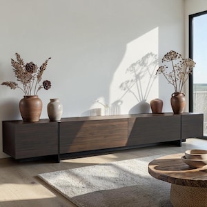 May include: A long, low-profile dark wood media console with a horizontal grain pattern, featuring four cabinet sections. The top surface holds two large brown ceramic vases with dried floral arrangements and one smaller light-colored ceramic vase.