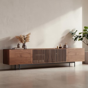 May include: A long, rectangular media console crafted from dark brown wood, featuring two solid end cabinets and two central cabinets with vertical slatted doors. The unit is supported by thin, black metal legs and has a smooth, flat top surface.