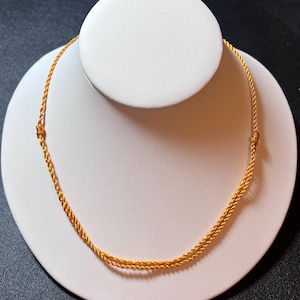 May include: A bright yellow cord necklace featuring a double-stranded twisted design. The necklace is constructed from a thin, braided cord material and includes two small, tied knots on either side to secure the structure of the circular loop.