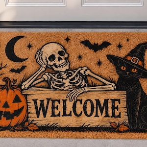 May include: A rectangular tan coir doormat featuring a black printed design of a skeleton leaning on a sign that reads WELCOME, a jack-o'-lantern, a black cat wearing a witch hat, a crescent moon, a bat, and a lit lantern in a dark style.
