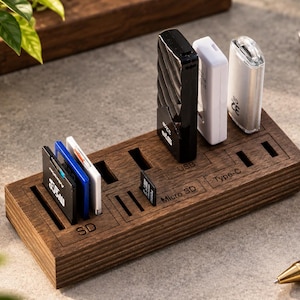 Puede incluir: Un organizador de almacenamiento rectangular de madera para tarjetas de memoria y unidades flash con etiquetas grabadas con láser para ranuras SD, Micro SD, USB y Tipo C. La base de madera marrón oscura sostiene varias tarjetas y tres unidades.