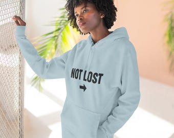 May include: A light blue hooded sweatshirt featuring the black text NOT LOST printed on the chest, positioned above a black right-pointing arrow. The garment includes a front kangaroo pocket, long sleeves with ribbed cuffs, and a matching drawstring hood.