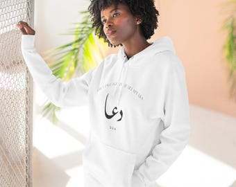 May include: A white long-sleeve hooded sweatshirt featuring a front graphic with the Arabic word for Dua, the English text The Language My Heart Speaks, and the word DUA printed in black ink. The garment includes a hood with drawstrings and a front pocket.