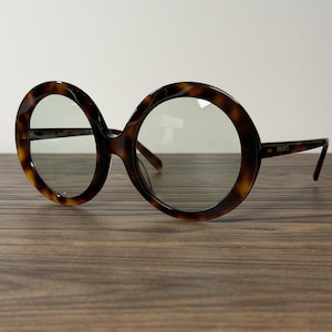 May include: Round eyeglasses with a brown and black tortoiseshell pattern frame. The temples feature the text PARIS, and the inner frame includes the text CELINE PARIS. The lenses are clear, and the overall design is circular and bold.