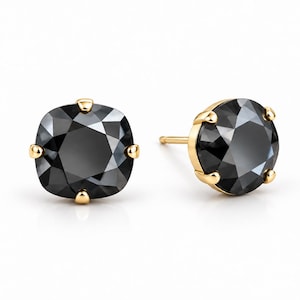 May include: A pair of stud earrings featuring faceted, cushion-cut black stones set in yellow gold. Each stone is secured by four gold prongs, with one earring shown from the front and the other angled to reveal the gold post and setting structure.
