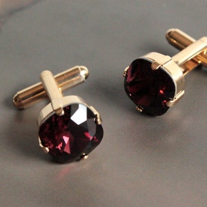 May include: A pair of gold cufflinks with a dark red, faceted gemstone in the centre of each cufflink.