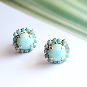May include: A pair of gold earrings with a light blue round gemstone surrounded by a halo of smaller turquoise blue gemstones.