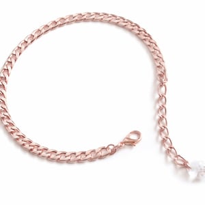 May include: Rose gold chain bracelet with a lobster clasp closure and a small extension chain. The bracelet features a curb chain design and a small, clear crystal charm at the end of the extension chain. The jewelry is displayed on a white background.