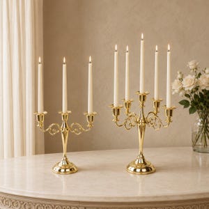 Puede incluir: Dos candelabros de metal dorado pulido con brazos curvos y bases circulares. El candelabro más pequeño sostiene tres velas cónicas de color crema, mientras que el más grande sostiene cinco velas cónicas de color crema, todas encendidas.