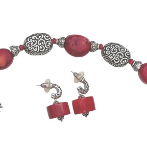 May include: A jewelry set featuring a bracelet and matching earrings. The bracelet has red oval beads and silver-colored, patterned beads. The earrings have red rectangular beads and silver-colored, curved posts. The set is on a white background.