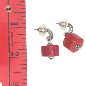 May include: A pair of earrings with a post back and a silver-tone curved design. Each earring features a red, rectangular-shaped stone. The earrings are approximately 1 inch in length.