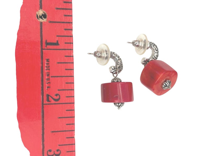 May include: A pair of earrings with a post back and a silver-tone curved design. Each earring features a red, rectangular-shaped stone. The earrings are approximately 1 inch in length.