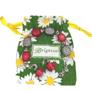 May include: A red and silver bracelet and matching earrings are displayed on a green daisy-print bag. The bag has a yellow ribbon drawstring and the brand name "Brighton" is visible on the bag.