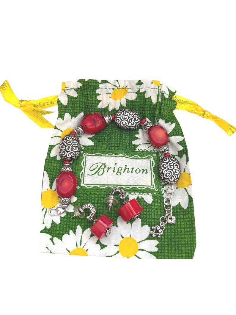 May include: A red and silver bracelet and matching earrings are displayed on a green daisy-print bag. The bag has a yellow ribbon drawstring and the brand name "Brighton" is visible on the bag.