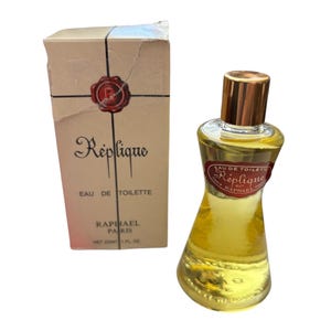 May include: A vintage bottle of Réplique Eau de Toilette perfume with its original box. The perfume bottle is a unique shape with a gold cap. The box is beige with the perfume name and logo printed on it. The bottle contains 1 fl oz of perfume.