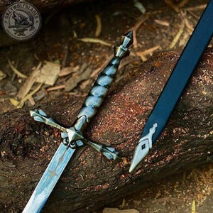 May include: A metal sword with a dark, segmented handle and a cross-shaped guard, featuring a blade with a light blue and white marbled pattern. Beside the sword lies a black scabbard with a silver-toned metal tip, marked with a small diamond.