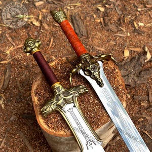 May include: Two decorative swords with metallic hilts and blades. One sword features a dark red wrapped handle and a skull-shaped crossguard. The other sword has a deep maroon handle and a crossguard with intricate dragon-like carvings.