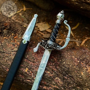 May include: A silver-toned rapier sword with a black leather-wrapped grip featuring silver studs, a decorative metal hilt, and a matching black scabbard with silver fittings. The blade is polished steel, and the pommel is rounded and metallic.