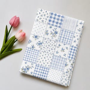 Könnte beinhalten: Ein rechteckiges Stoffstück mit einem Patchwork-Design aus blauen und weißen Mustern, darunter Blumenprints, Vichy-Karos, Streifen und Punkte, präsentiert neben zwei rosa Tulpen mit grünen Stielen und Blättern.