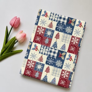 May include: A rectangular fabric piece featuring a patchwork design of squares in red, navy blue, and cream. The pattern includes illustrations of Christmas trees, snowflakes, holly berries, and plaid motifs arranged in a repeating grid layout.