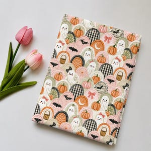 May include: A rectangular fabric piece featuring a repeating pattern of ghosts, pumpkins, bats, and rainbows in shades of orange, pink, green, and black. The design includes small bows and baskets, with two pink tulips positioned to the left side.