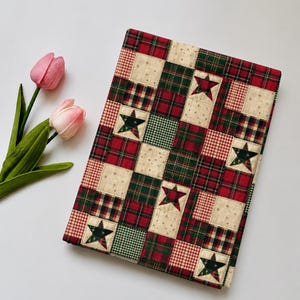 May include: A rectangular fabric quilt featuring a patchwork design of red, green, and cream squares. The pattern includes various plaid and gingham prints interspersed with cream squares decorated with small gold stars and dark green fabric stars.