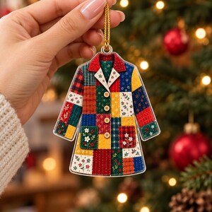 Könnte beinhalten: Ein flacher, mantelartiger Weihnachtsbaumschmuck mit einem bunten Patchwork-Design. Das Muster besteht aus verschiedenen Quadraten in Rot, Grün, Gelb und Blau, die mit Blumen- und geometrischen Motiven verziert sind. Es hat vier Knöpfe und zwei Taschen.