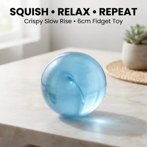 May include: A light blue spherical fidget toy with a smooth, translucent surface. The text above the object reads SQUISH • RELAX • REPEAT and Crispy Slow Rise • 6cm Fidget Toy. The sphere is a solid, uniform colour and features a subtle swirl detail.