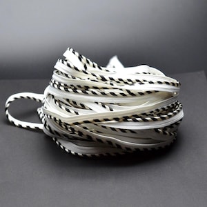 May include: A continuous coil of zipper tape featuring a white center track flanked by edges with a black and white diagonal striped pattern. The long length of fastener material is wound into a dense, circular bundle with a loose loop extending out.