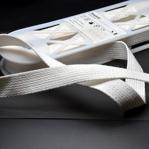 May include: A spool of off-white cotton and polyester twill tape featuring a herringbone weave pattern. The white plastic spool includes a label with the brand name Simplicity, care instructions, and the text 1 inch by 10 yards / 9.1 m.