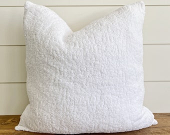 May include: White fluffy pillow with a soft, textured surface. The pillow is sitting on a wooden surface.
