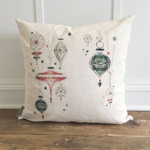 May include: A white throw pillow with a vintage Christmas ornament design. The ornaments are red, green, and gold with a white background. The pillow is perfect for adding a festive touch to your home decor.